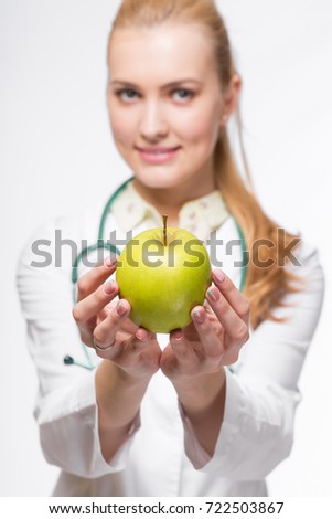 Portrait of cute female doctor giving apple at camera isolated on a white background