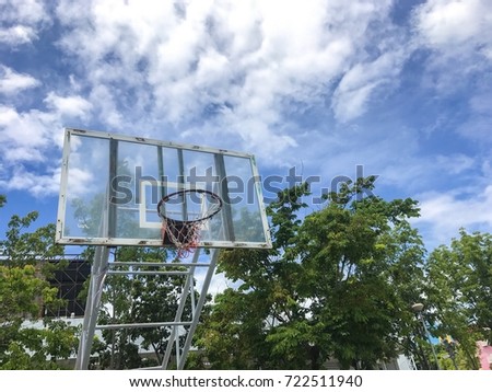 Basketball hoop in the park with white cloud ,blue sky and green trees as background.