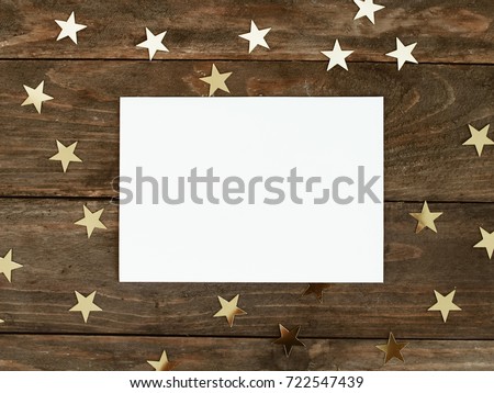 Mock up greeting card on wood rustic background with Christmas gold stars confetti. Invitation, paper. Place for text flat lay
