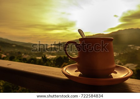 A beautiful cup of coffee or tea set is on the balcony in the light of the rising sun with beautiful nature in morning.
