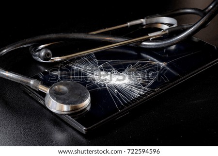 Broken tablet with broken screen and stethoscope in repair. Black table. Black background