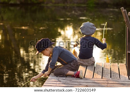 Laughing children siting with sticks in hands on the river bank