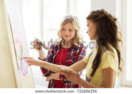 art school, creativity and people concept - happy student girls or artists with easel, palettes and paint brush painting still life picture at studio