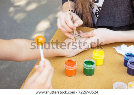 Artist draws a pattern on the child's hand with a brush and watercolor orange paint. Hand painting children activity. Animator draws the painting on the child hand