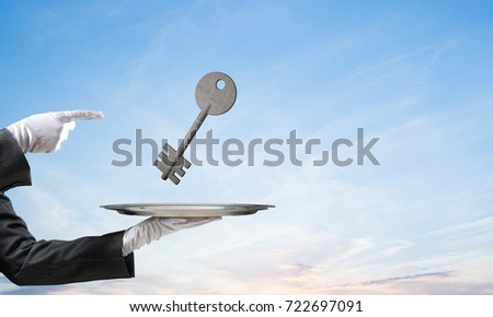 Closeup of waiter's hand in white glove presenting stone key symbol on metal tray and pointing on it with blue cloudy skyscape on background. 3D rendering.