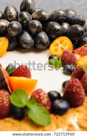 Festive cake with grapes, figs and kumquat in gold candurin on white background Picture for a menu or a confectionery catalog.