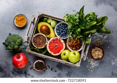 Healthy food clean eating selection in wooden box: fruit, vegetable, seeds, superfood, cereals, leaf vegetable on gray concrete background