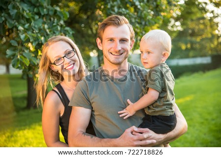Young happy smiling family in green garden or city park. Beautiful mom, handsome dad and their cute little baby boy, all with blue eyes and fair hair. Forever young concept photo.