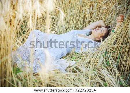 fashion, style. beautiful woman in a white dress lies in the ears of corn on a wheat field