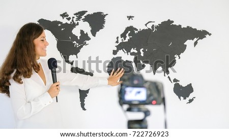 The journalist is reporting on the background of a large map of the world in front of the camera.