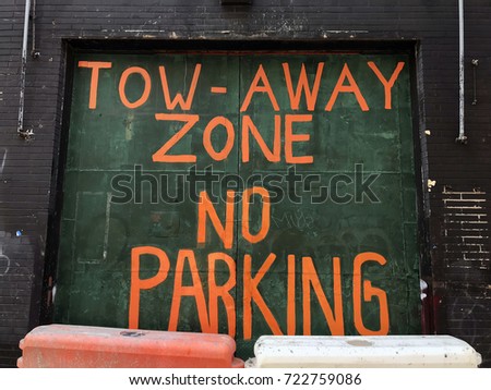 Tow-Away Zone No Parking in orange on green wall with construction blockades on a city street.