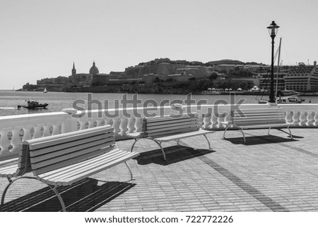 Colorful park benches on the embankment of Valletta. Promenade on the background of the bay in Malta. Black and white picture