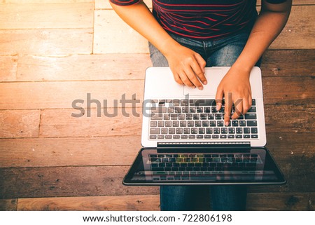 Young woman working on laptop computer while sitting on the wooden floor with sunlight, vintage tone. Royalty-Free Stock Photo #722806198