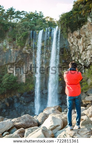 A man standing in front of a Beautiful natural Jeongbang Falls and taking pictures. The only waterfall in Asia to fall directly into the ocean. Seogwipo, Jeju, South korea, Asia.