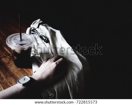 The picture of A cup of iced Amricano, hand, watch, glasses and white suit on wooden table. Coffee and Hipster concept