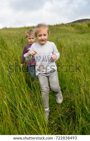 portrait Happy Young boy and girl jogging running in tall grass in ireland irish nature on an adventure hike in summer.