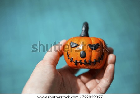 Halloween pumpkin in girl hand over blurred blue water background, outdoor day light