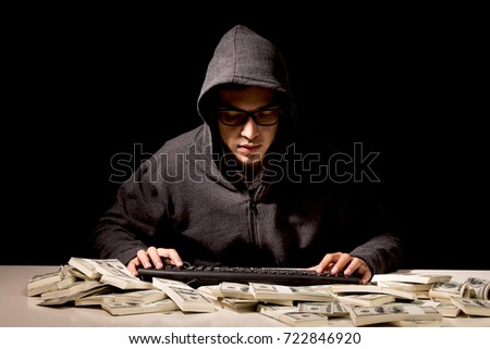 Hacker in a hood stealing information with computer on dark background