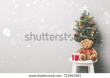 Lovely Christmas holiday background with red gift boxes, teddy bear, small decorated Pine tree and falling snow in white gray room