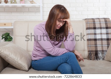 Sad middle age woman sitting on a sofa in the living room. Menopause Royalty-Free Stock Photo #722864833