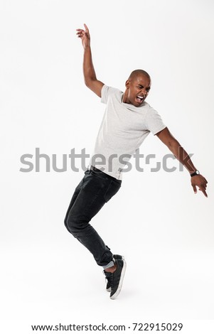 Photo of emotional young african man dancing isolated over white background. Looking aside.