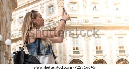Pretty tourist teenager taking a photo with her mobile phone in the Vittorio Emanuele shopping arcade in Milan, Italy