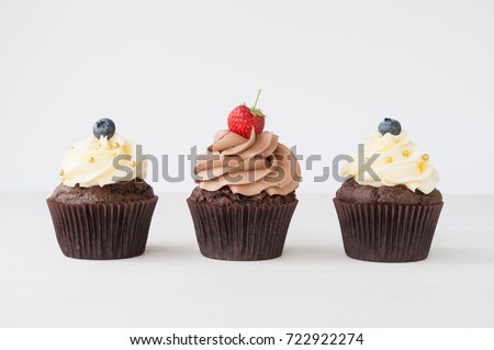 Cupcakes with whipped chocolate and vanila cream, decorated fresh strawberry, blueberry, gold confectionery sprinkling on white wooden table. Picture for a menu or a confectionery catalog.