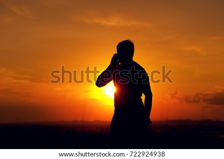 Silhouette of young man talking on the phone, enjoying sunset time outdoors. Travelling and vacation concept.