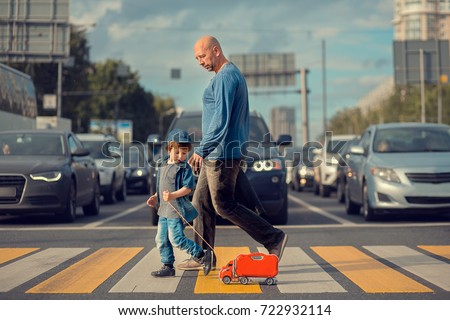 Little boy with his father and a red toy track are crossing the street on crosswalk. A lot of cars are waiting them. Image with selective focus and toning Royalty-Free Stock Photo #722932114