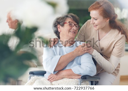 Old lady in glasses sitting in a wheelchair and smiling at her nurse Royalty-Free Stock Photo #722937766