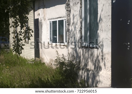 Old gray wall of a house with shadows of trees, windows. Summer texture