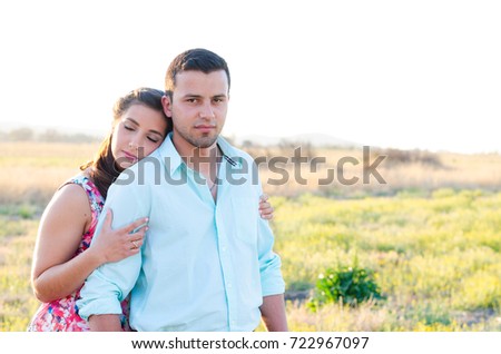 Couple standing together in a field with the woman's head resting against the man's shoulder, with her eyes closed