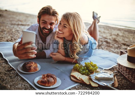 Photo of young couple taking a selfie with mobile phone on picnic.