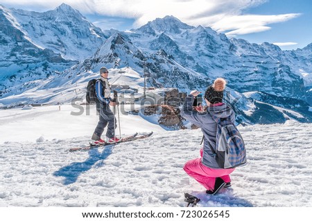 The girl takes a photograph of the skier on the iPhone in the background of the Swiss Alps.

