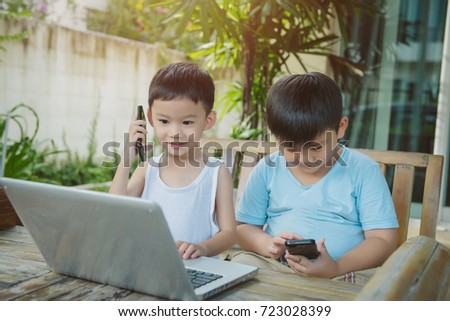 Portrait two brothers playing computer games  and making phone call on  wood table  in the backyard. Two boy using laptop and smartphone.