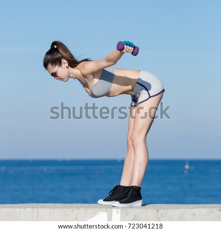 Female fitness outdoors. Girl with dumbbells exercising on seafront