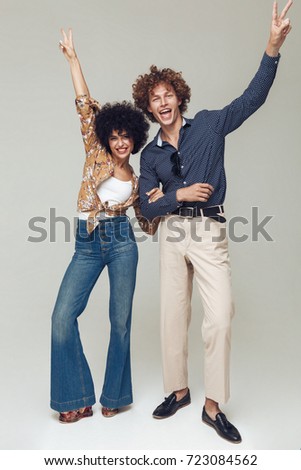 Photo of young emotional retro loving couple standing and posing isolated. Looking camera showing peace gesture.
