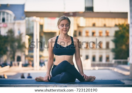 Beautiful young woman practices yoga asana Cow Face pose gomukhasana in the city