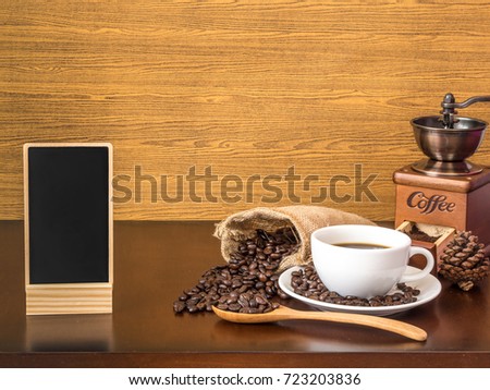 White cup coffee with coffee beans, coffee grinder and blank chalk board on wooden top table 