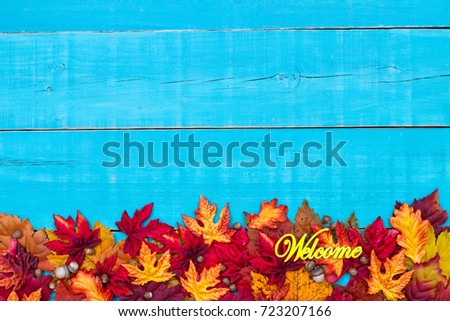 Welcome sign with colorful fall leaves border and antique rustic teal blue wood background; autumn, Thanksgiving, Halloween, seasonal nature sign with painted wooden copy space