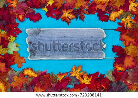 Colorful fall leaves border with blank wood sign hanging on antique rustic teal blue wooden background; autumn, Thanksgiving, Halloween, seasonal nature background with copy space