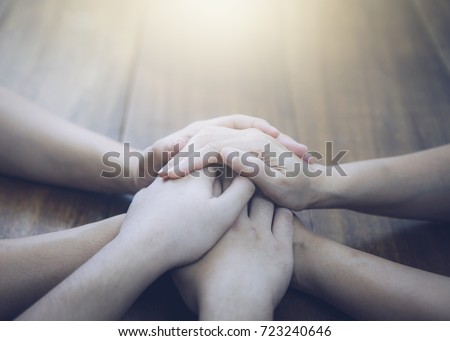 Three  people are joining  hands and pray together on wooden table  with the light from above, copy space 