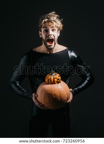 Halloween macho holding two pumpkins on dark background. Scared man shouting in black costume. Autumn and harvest season. Holidays celebration concept. Trick or treat.