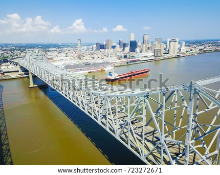 Aerial view of Crescent City Connection and riverside Downtown New Orleans again cloud blue sky. Overhead view the cantilever bridges and an empty cargo container ship on Mississippi river.