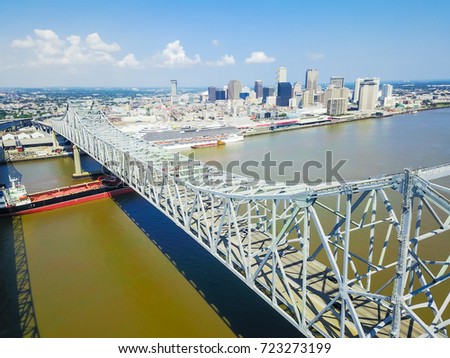 Aerial view of Crescent City Connection and riverside Downtown New Orleans again cloud blue sky. Overhead view the cantilever bridges and an empty cargo container ship on Mississippi river.