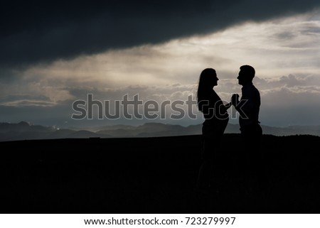 Silhouette of pregnant couple against dark sky.