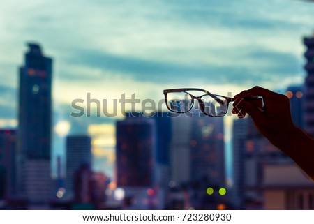 Male hand holding glasses against night cityscape.Night cityscape focused in glasses lenses.