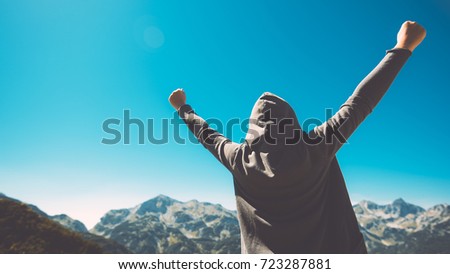 Winning and success. Victorious female person standing on mountain top with arms raised in V. Achievement and accomplishment in life. Toned image. Royalty-Free Stock Photo #723287881