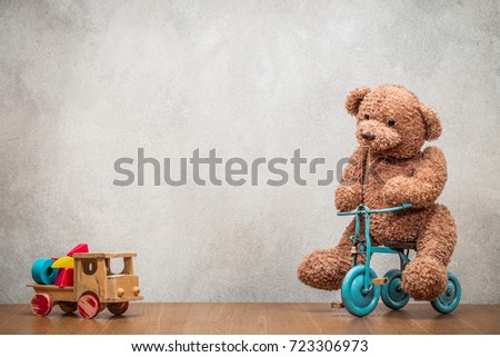 Teddy Bear sitting on old retro toy tricycle and obsolete classic wooden truck with construction blocks front concrete textured wall background. Vintage instagram style filtered photo