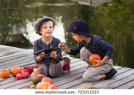 Laughing children paint small Halloween pumpkins on the river bank